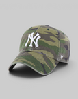 A baseball cap in a green and brown camouflage pattern, featuring a white embroidered New York Yankees logo on the front and a small white '47 brand logo on the side, set against a solid gray background.