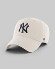 An off-white baseball cap featuring a navy blue embroidered New York Yankees logo on the front and a small navy '47' brand logo on the side, set against a solid gray background.
