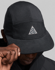 Nike ACG Fly Cap Black Reflective Silver HJ7021-010 — front product shot showing black five-panel cap with detachable perforated cape featuring reflective ACG triangle logo on front panel