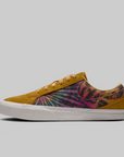 A low-top skate shoe shown in profile against a solid gray background. The shoe features a mustard yellow suede toe and laces, a side panel with a colorful tie-dye pattern in pink, purple, blue, and black, and a thick white rubber sole.