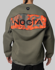 Back view of a person wearing an olive green pullover sweatshirt with a large orange and gray graphic panel across the upper back featuring the word NOCTA in black.
