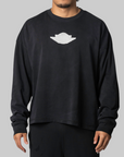 A man wearing a black long-sleeve crewneck sweatshirt with a white UFO graphic on the chest, photographed against a solid gray background.