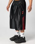 A person wearing black Adidas athletic shorts with red three-stripes and a red trefoil logo, styled with white socks and black sneakers against a light gray studio background.