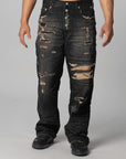 A person modeling a pair of heavily distressed black denim jeans with ripped details showing tan inner lining, photographed against a light gray studio background.