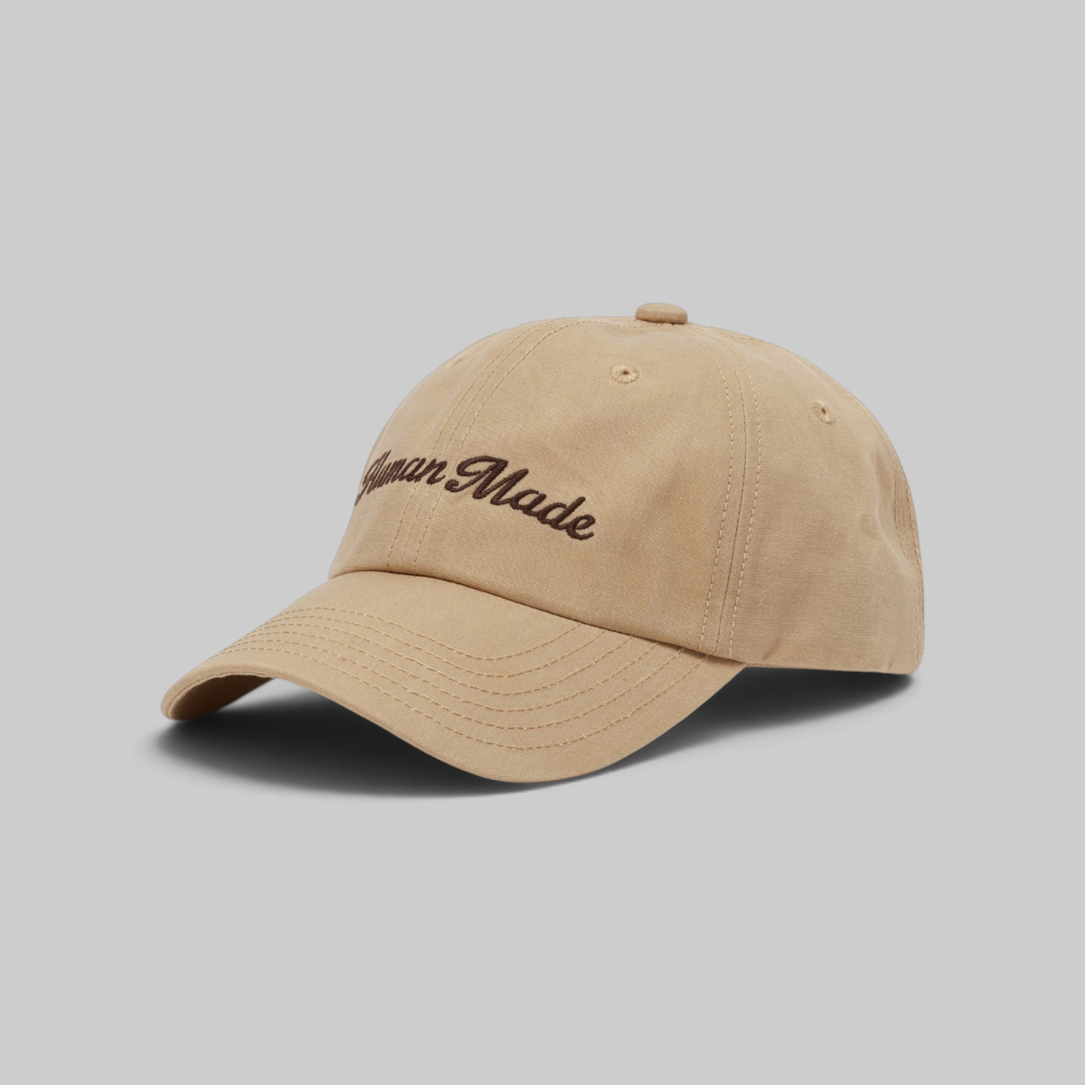 A beige cotton baseball cap with 'American Made' embroidered in brown script on the front, photographed on a solid gray background.