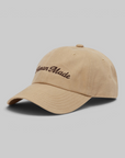 A beige cotton baseball cap with 'American Made' embroidered in brown script on the front, photographed on a solid gray background.