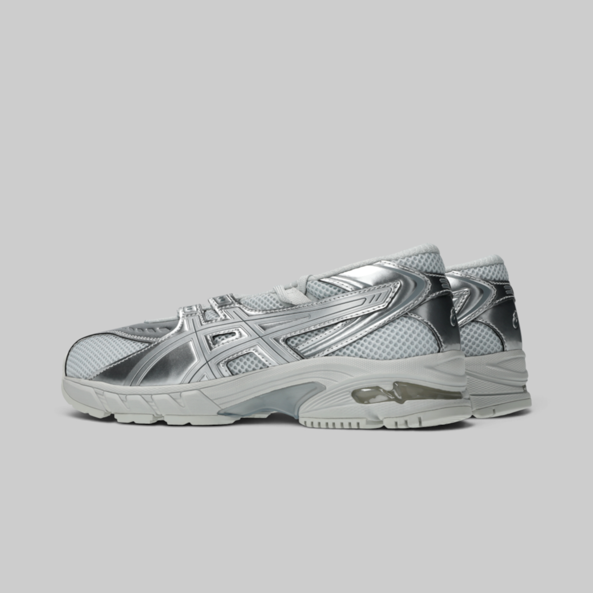 A pair of metallic silver athletic sneakers with mesh panels and reflective synthetic overlays, shown from a side profile view against a solid gray background.