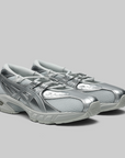 A pair of ASICS Gel-Kayano running shoes in metallic silver and light gray, shown from a three-quarters angle on a solid gray background.