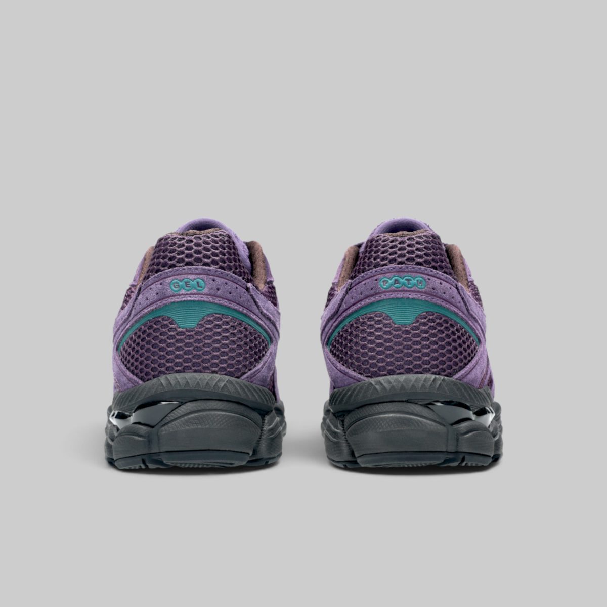 A pair of purple running shoes shown from the back, featuring a purple mesh upper, a teal accent panel, and a dark gray sole, set against a solid gray background.