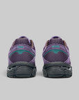 A pair of purple running shoes shown from the back, featuring a purple mesh upper, a teal accent panel, and a dark gray sole, set against a solid gray background.