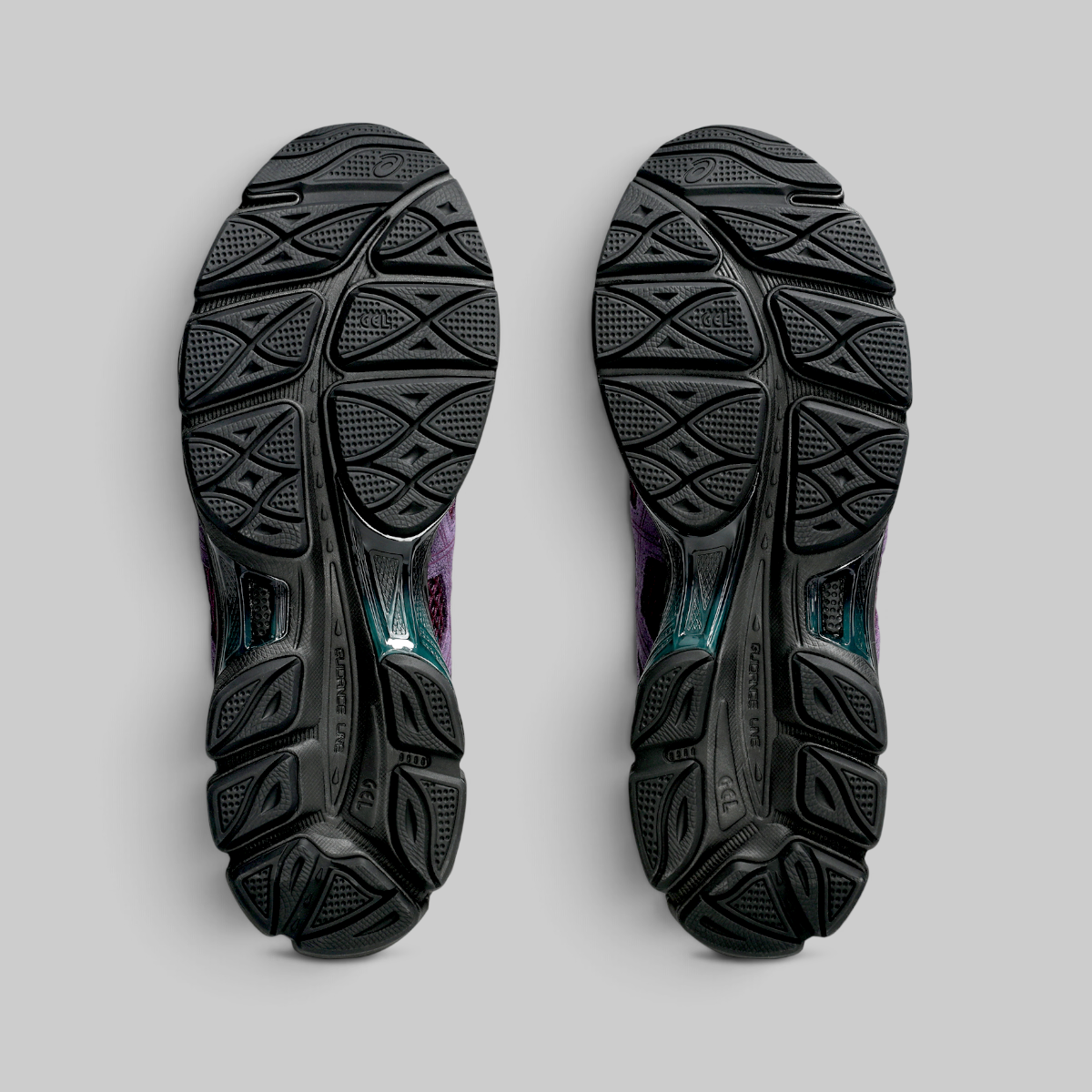The outsoles of a pair of running shoes, shown from a top-down view against a neutral gray background. The outsoles are solid black with a textured, geometric tread pattern.