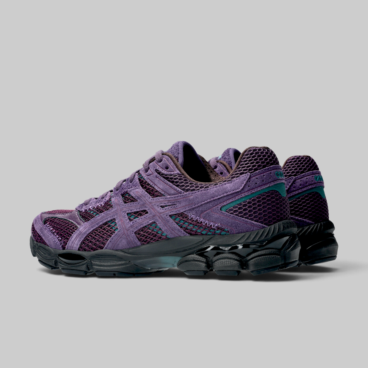 A pair of ASICS running shoes in purple and black, featuring the brand's signature side stripe design, shown against a neutral gray background.