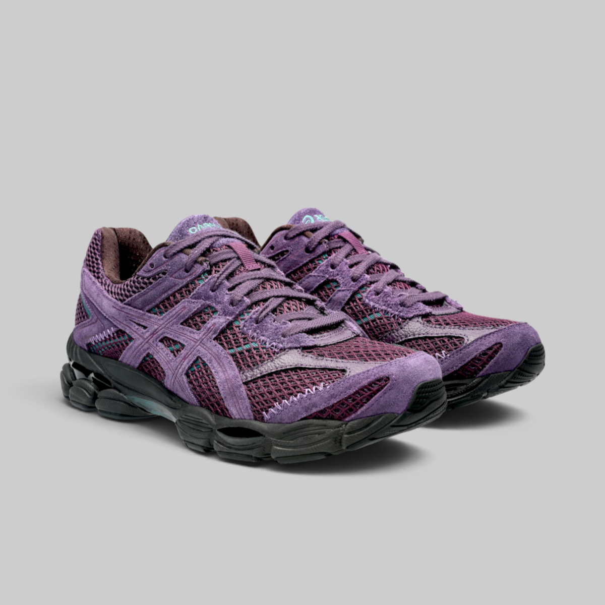 A pair of Asics running shoes in a purple and burgundy mesh and suede upper, with black and gray cushioned soles, photographed on a solid gray background.