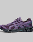 A single ASICS sneaker in purple and dark gray, shown from a side profile against a solid gray background.