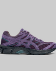 A single running shoe in purple suede and mesh with dark gray and teal accents, shown in a side profile on a solid gray background.