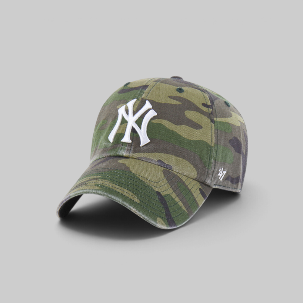 A baseball cap in a green and brown camouflage pattern, featuring a white embroidered New York Yankees logo on the front and a small white '47 brand logo on the side, set against a solid gray background.