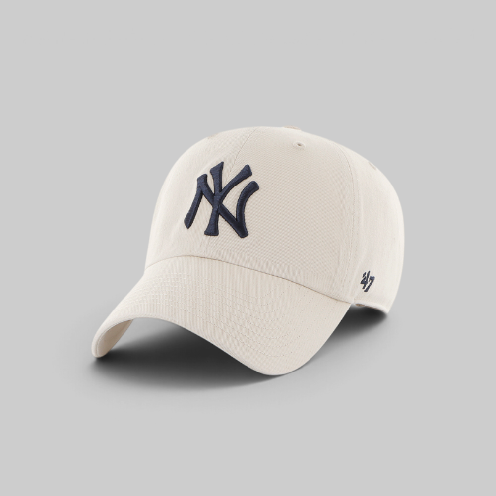An off-white baseball cap featuring a navy blue embroidered New York Yankees logo on the front and a small navy '47' brand logo on the side, set against a solid gray background.