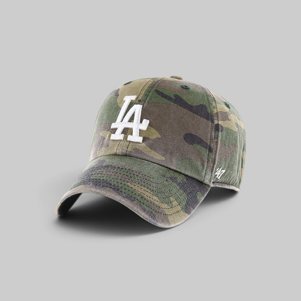 A baseball cap in a green and brown camouflage pattern, featuring a white embroidered 'LA' logo on the front and a small white '47' brand logo on the side, set against a solid gray background.