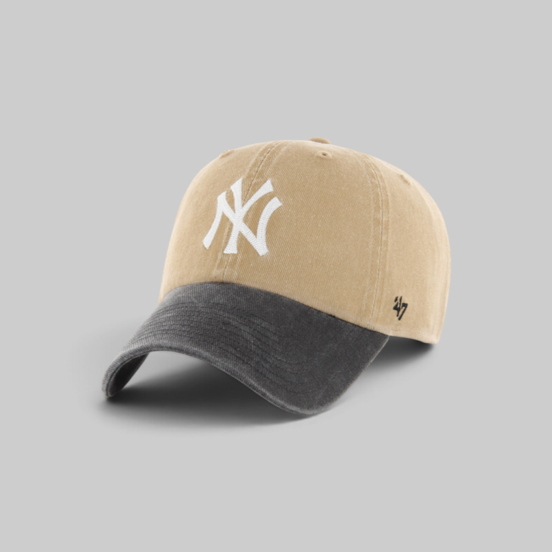 A baseball cap with a tan crown, a dark gray curved brim, a white embroidered New York Yankees logo on the front, and a small black '47 brand logo on the side, shown on a neutral gray background.