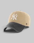 A baseball cap with a tan crown, a dark gray curved brim, a white embroidered New York Yankees logo on the front, and a small black '47 brand logo on the side, shown on a neutral gray background.