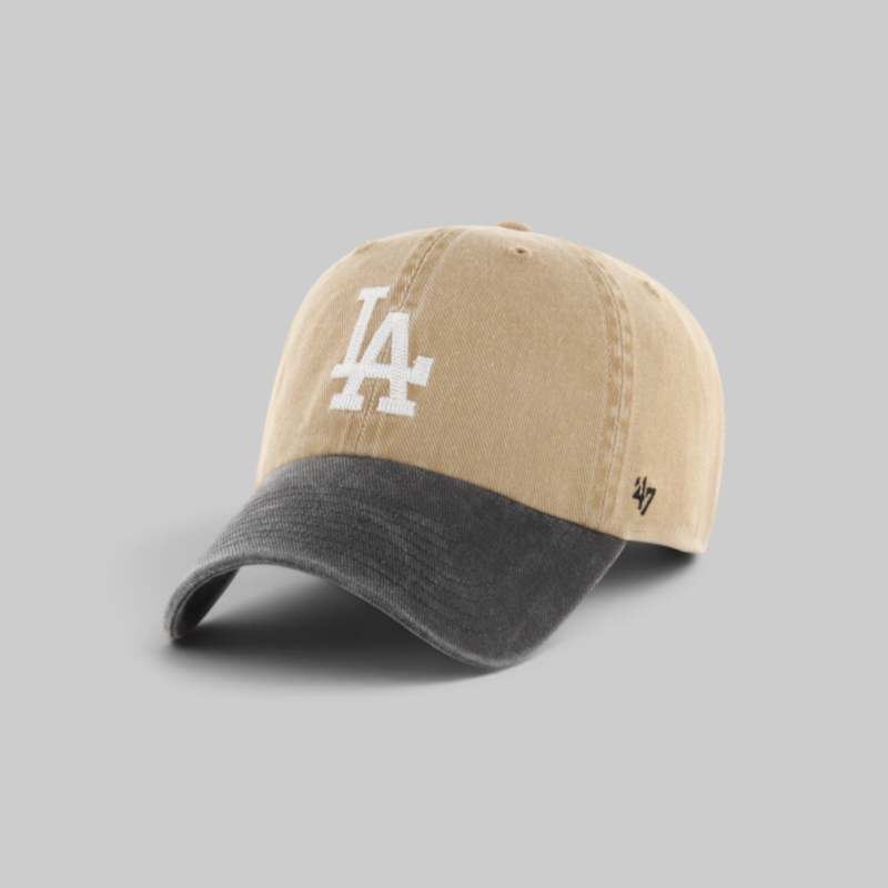 A baseball cap with a beige washed cotton crown, a dark gray curved brim, a white embroidered 'LA' logo on the front, and a small black '47' brand logo on the side, shown on a neutral gray background.