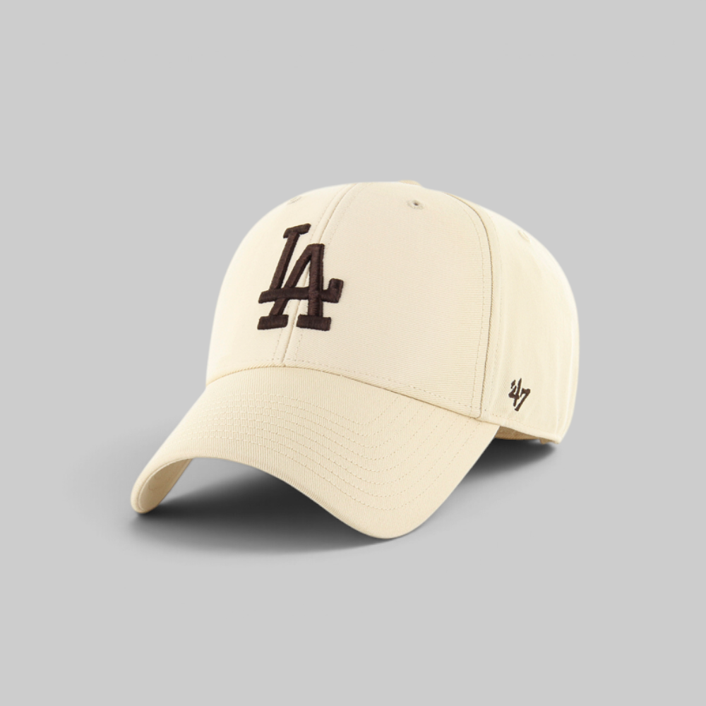 A cream-colored baseball cap featuring a black embroidered 'LA' logo on the front and a black '47' brand logo on the side, set against a solid gray background.