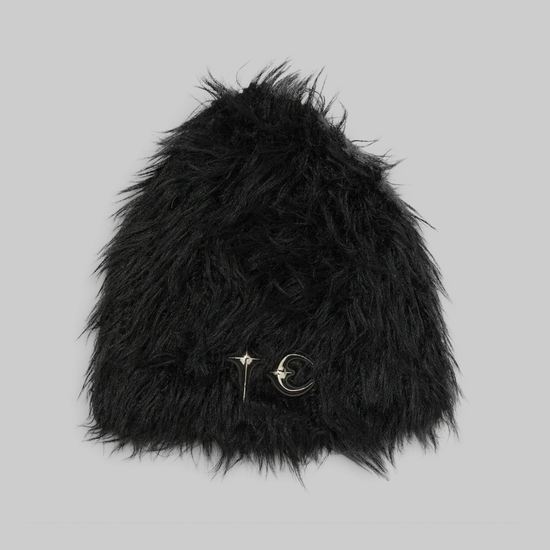 A black shaggy faux fur beanie hat featuring two small gold-toned metal pins, one with a star and one with a crescent moon and star, on the front, set against a solid light gray background.