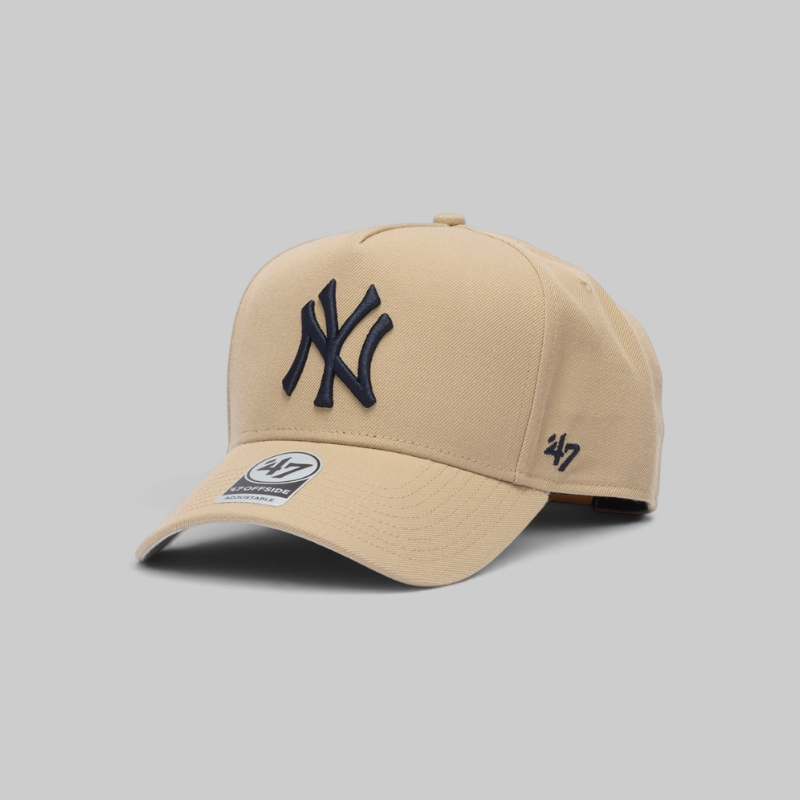 A beige New York Yankees baseball cap by '47, featuring an embroidered navy blue NY logo on the front and a '47 logo on the side, set against a solid gray background.