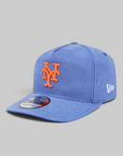 A blue New York Mets fitted baseball cap by New Era, featuring an orange embroidered 'NY' logo on the front and a white New Era flag logo on the side, set against a solid gray background.