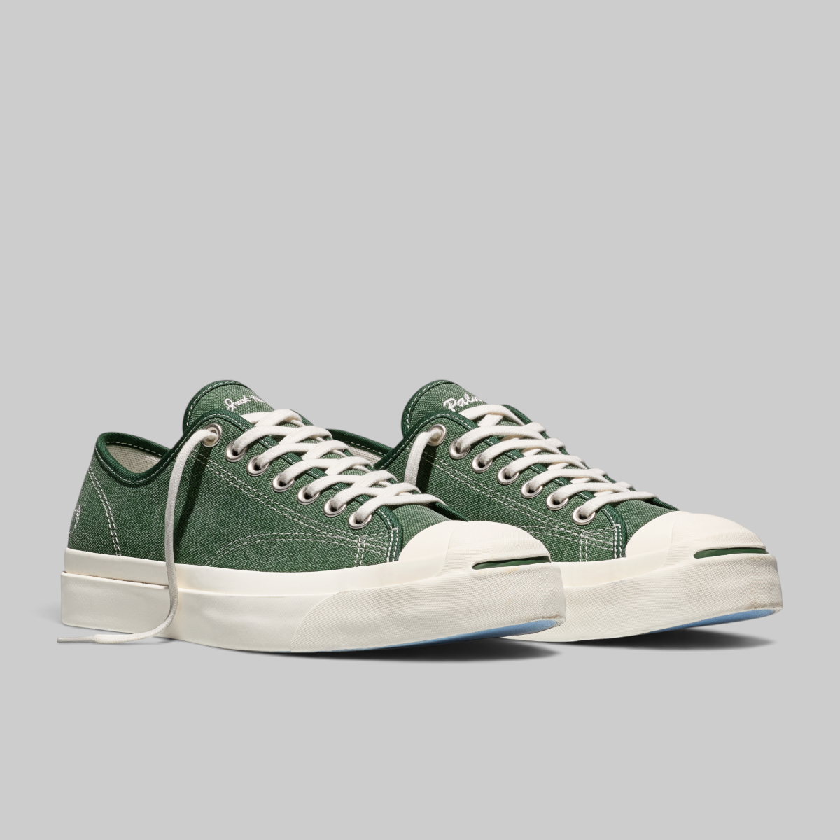 A pair of green canvas low-top sneakers with white laces, white rubber toe caps, and thick white platform soles, photographed on a solid gray background.