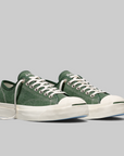 A pair of green canvas low-top sneakers with white laces, white rubber toe caps, and thick white platform soles, photographed on a solid gray background.