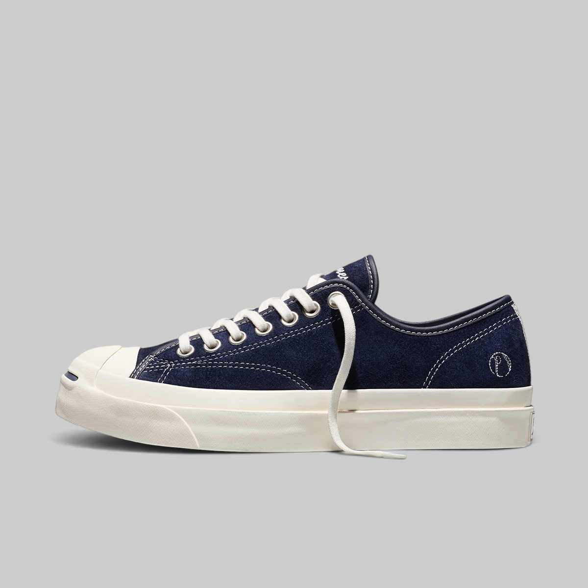 A navy blue canvas low-top sneaker with white laces, a white rubber toe cap, and a thick white platform sole, shown in profile against a solid gray background.