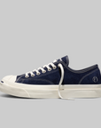 A navy blue canvas low-top sneaker with white laces, a white rubber toe cap, and a thick white platform sole, shown in profile against a solid gray background.