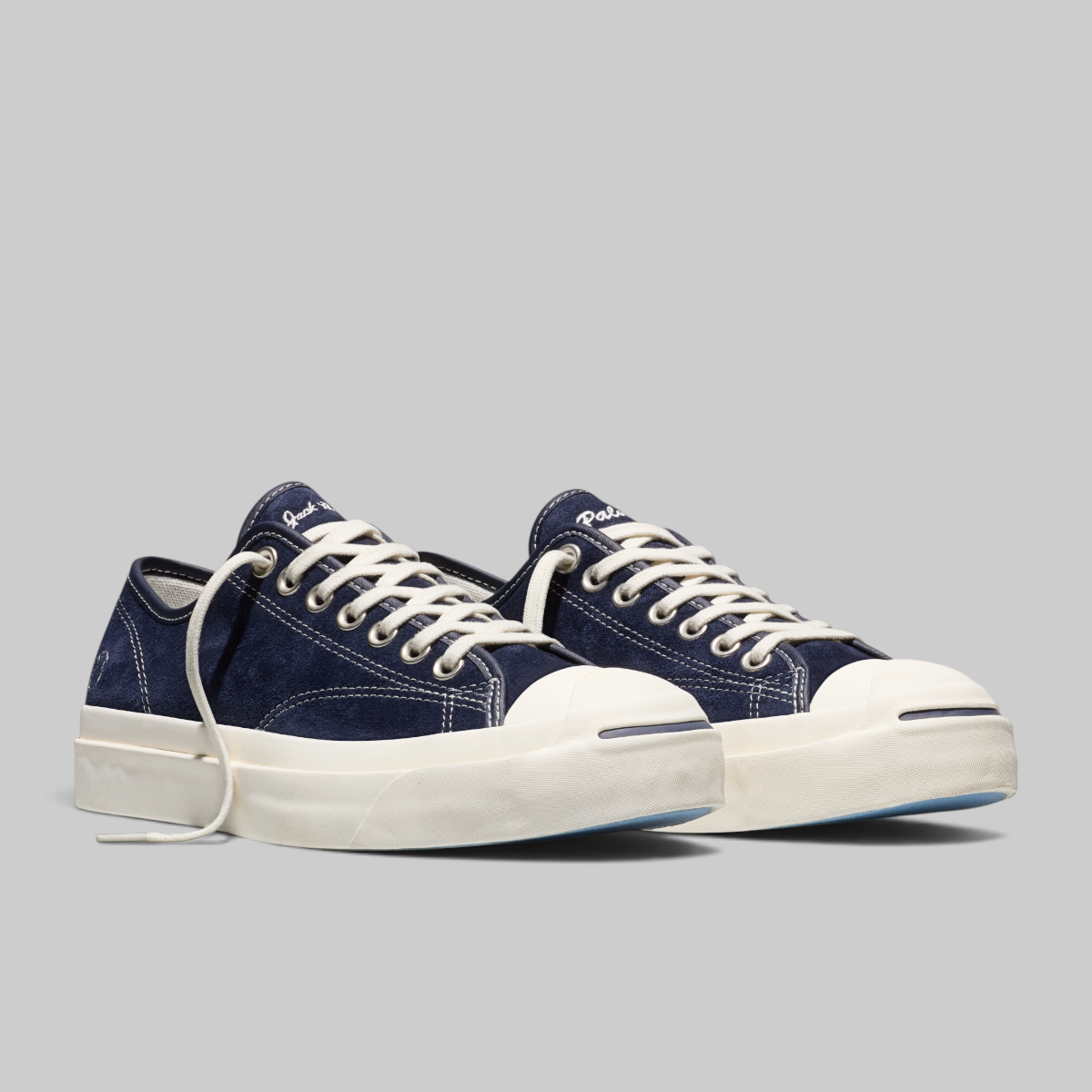 A pair of low-top sneakers in navy blue canvas with white laces, white rubber toe caps, and thick white platform soles, photographed on a solid light gray background.