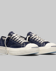 A pair of low-top sneakers in navy blue canvas with white laces, white rubber toe caps, and thick white platform soles, photographed on a solid light gray background.