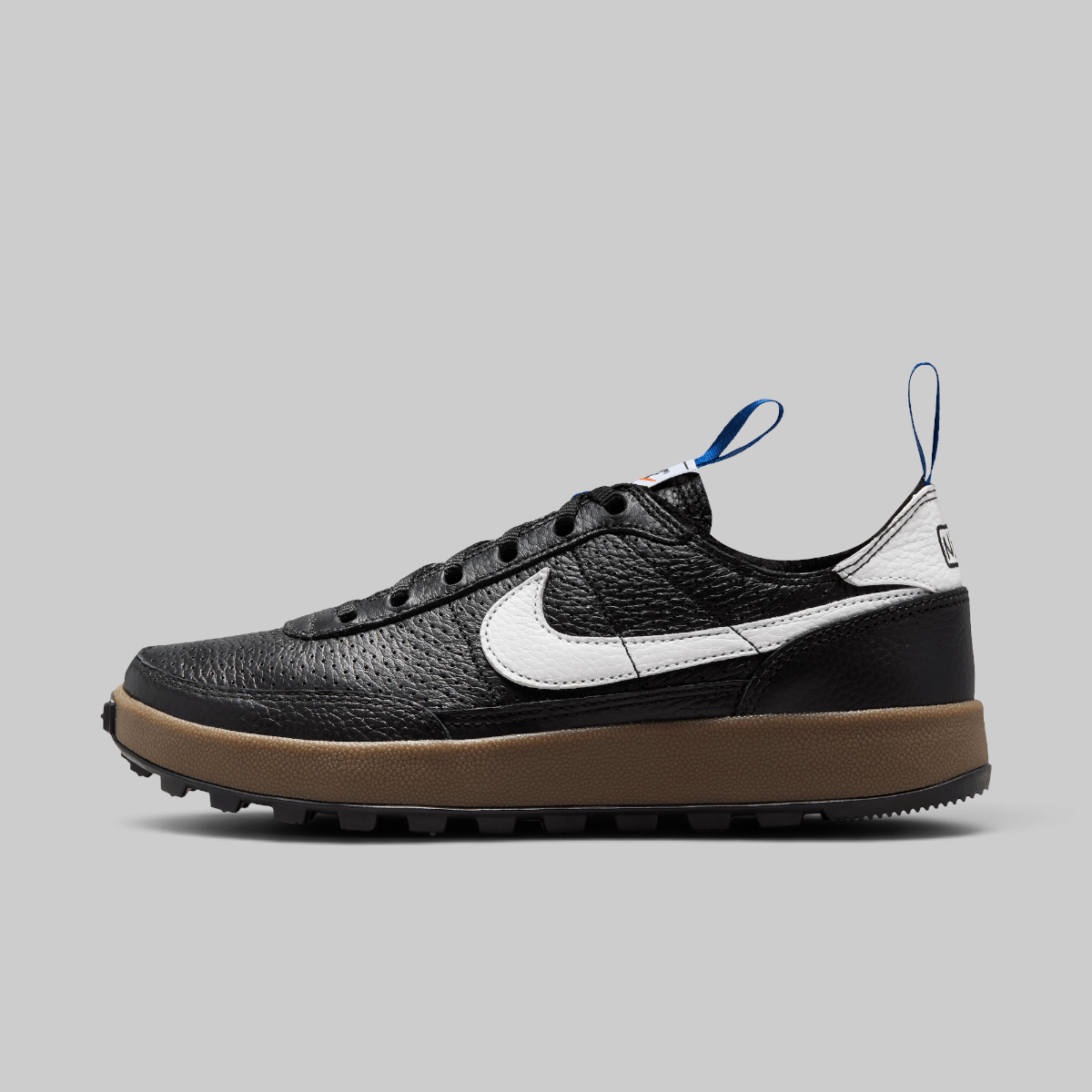 A Nike low-top sneaker in black textured leather with a white Swoosh, a thick brown gum sole, and blue pull tabs, shown in a side profile on a light gray background.