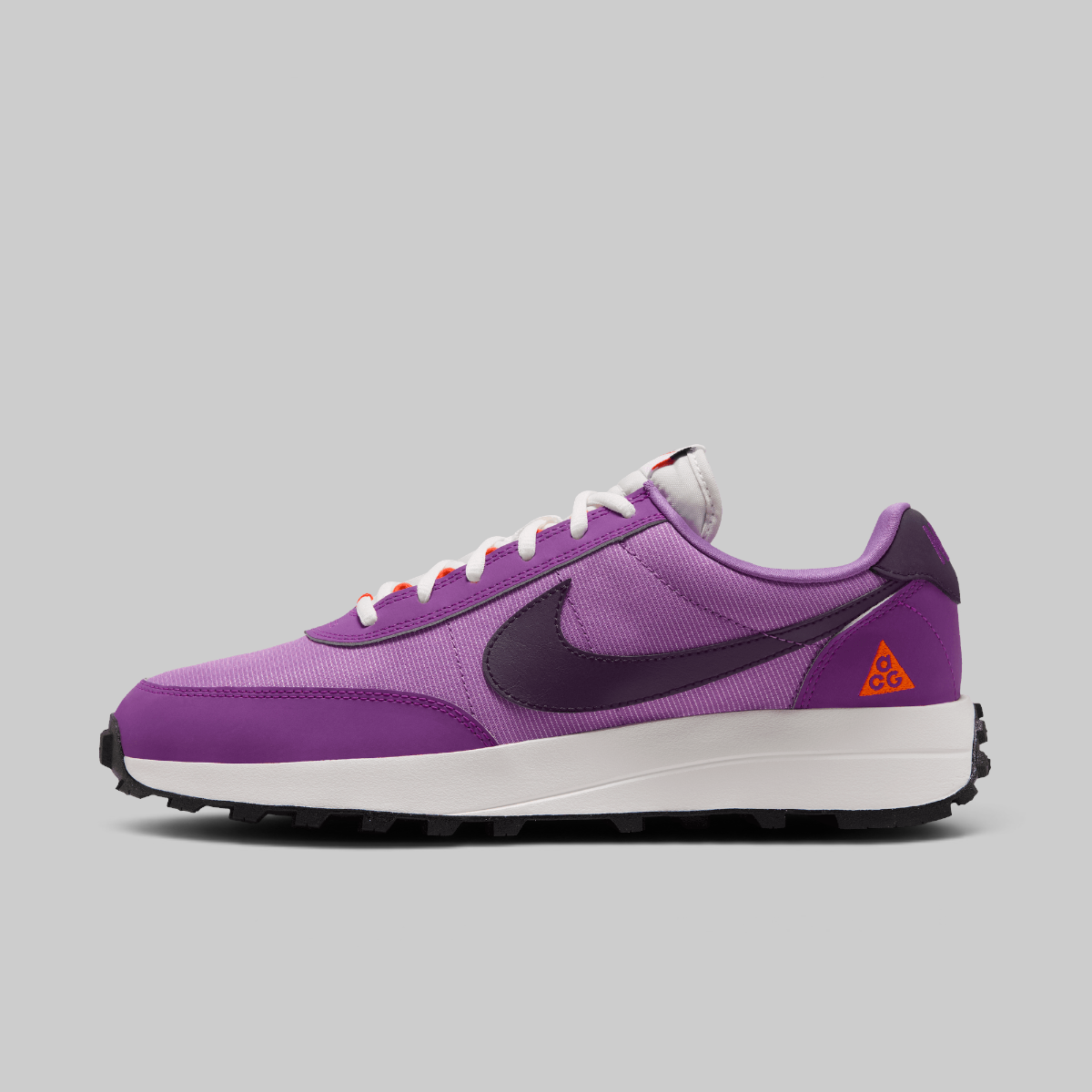 A Nike ACG LDV sneaker in purple, featuring a purple mesh and suede upper, a dark purple Swoosh, a white midsole, and a small orange Tri-A-Vec logo on the heel, shown against a solid gray background.