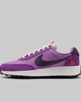 A Nike ACG LDV sneaker in purple, featuring a purple mesh and suede upper, a dark purple Swoosh, a white midsole, and a small orange Tri-A-Vec logo on the heel, shown against a solid gray background.