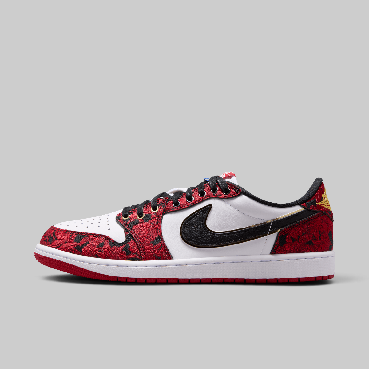 A Nike Air Jordan 1 Low sneaker in red, white, and black, featuring a red and black patterned leather upper, a black Swoosh, and a white midsole, shown against a solid gray background.
