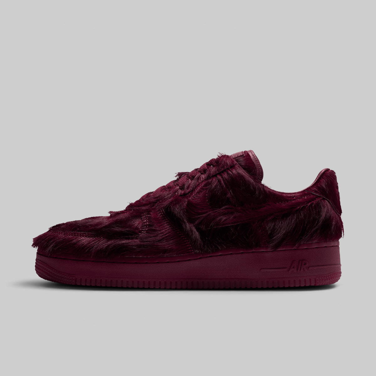A single low-top sneaker in a deep burgundy faux fur material, shown from a side profile against a solid light gray background.
