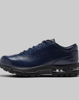 A navy blue Nike sneaker with a crocodile-embossed leather upper, black laces, and a black sole with visible air cushioning units, shown against a solid gray background.