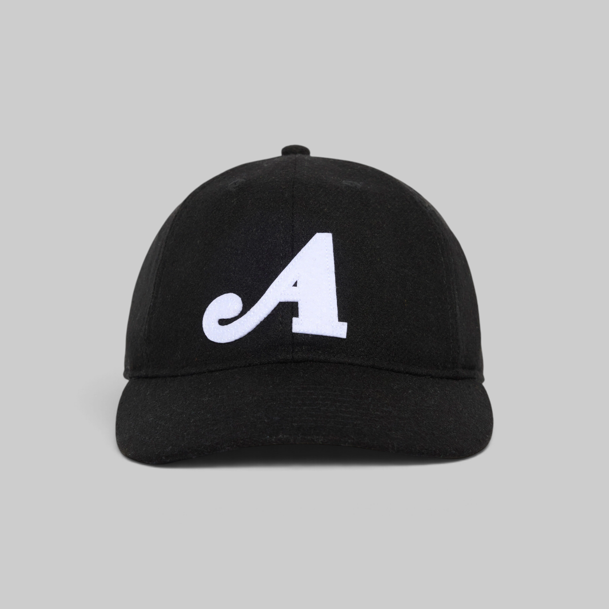 A black baseball cap with a white embroidered script letter 'A' on the front, photographed against a solid light gray background.