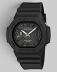 A G-Shock analog watch with a matte black resin case and strap, featuring a black dial with silver hands and small yellow accents.