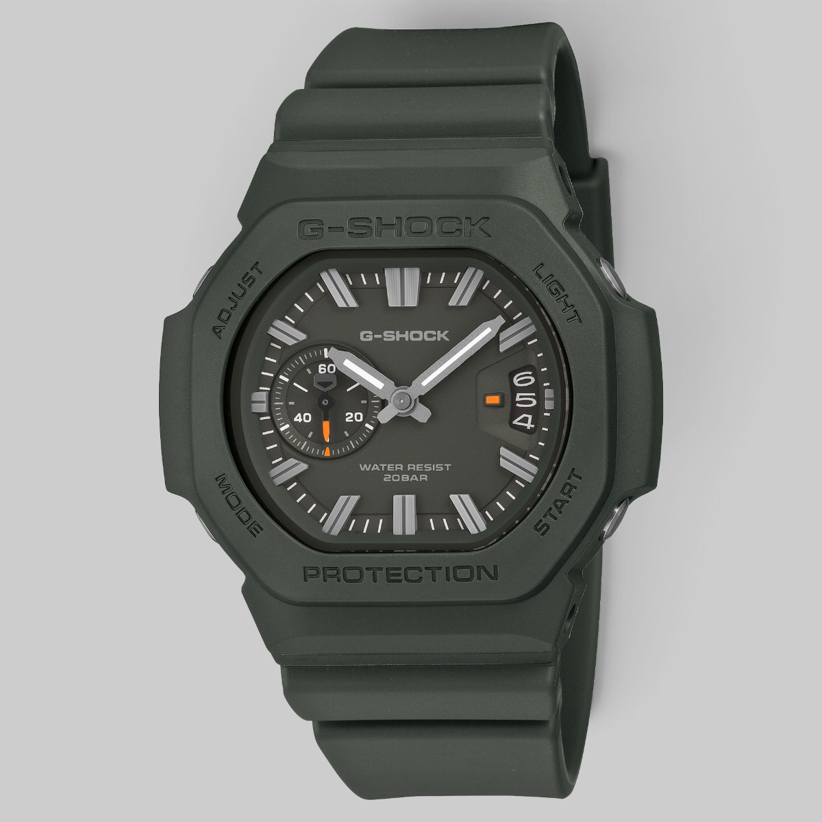A G-Shock watch in matte olive green with a dark gray dial, featuring silver hands and white hour markers, set against a solid light gray background.