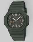 A G-Shock watch in matte olive green with a dark gray dial, featuring silver hands and white hour markers, set against a solid light gray background.