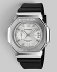 A G-Shock watch with a brushed silver-tone metal case, white dial, and black textured strap, shown on a neutral gray background.