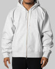 A man wearing a light gray zip-up hoodie with a drawstring hood and kangaroo pockets, shown from the chin down against a plain light gray background.