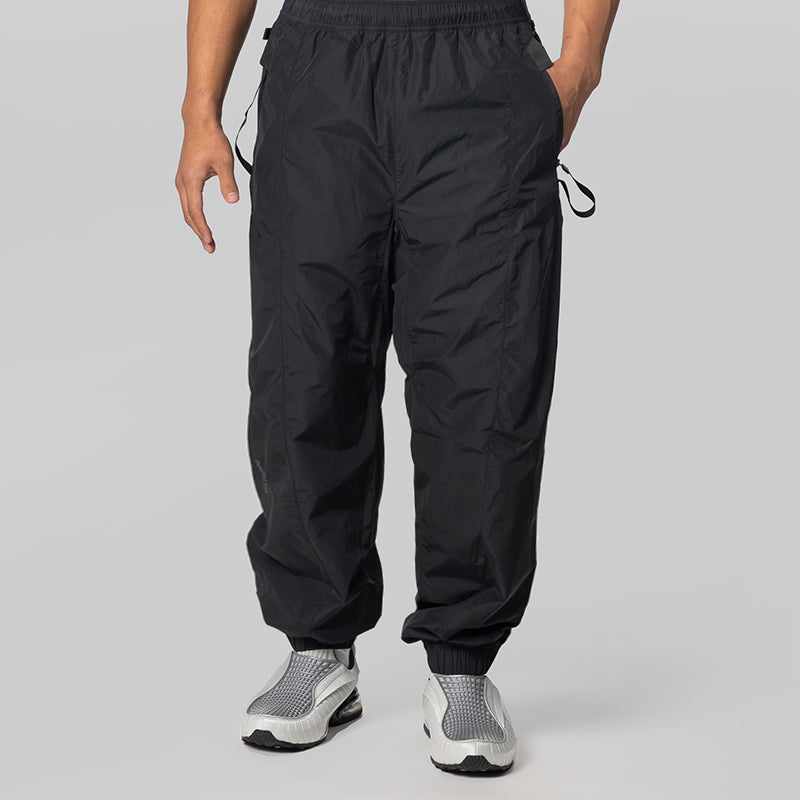 Black lightweight jogger-style pants with an elastic waistband and drawstring details, shown on a model from the waist down against a light gray studio background.