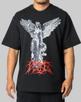 A man wearing a black oversized t-shirt with a large graphic print of a silver winged statue and red stylized text on the front, set against a solid gray background.