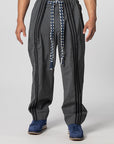 A person wearing dark gray baggy pants with black side stripes, a blue and white braided drawstring, and blue sneakers, shown from the waist down on a light gray studio background.